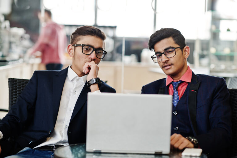Two indian business man in suits sitting at office on cafe and looking at laptop.